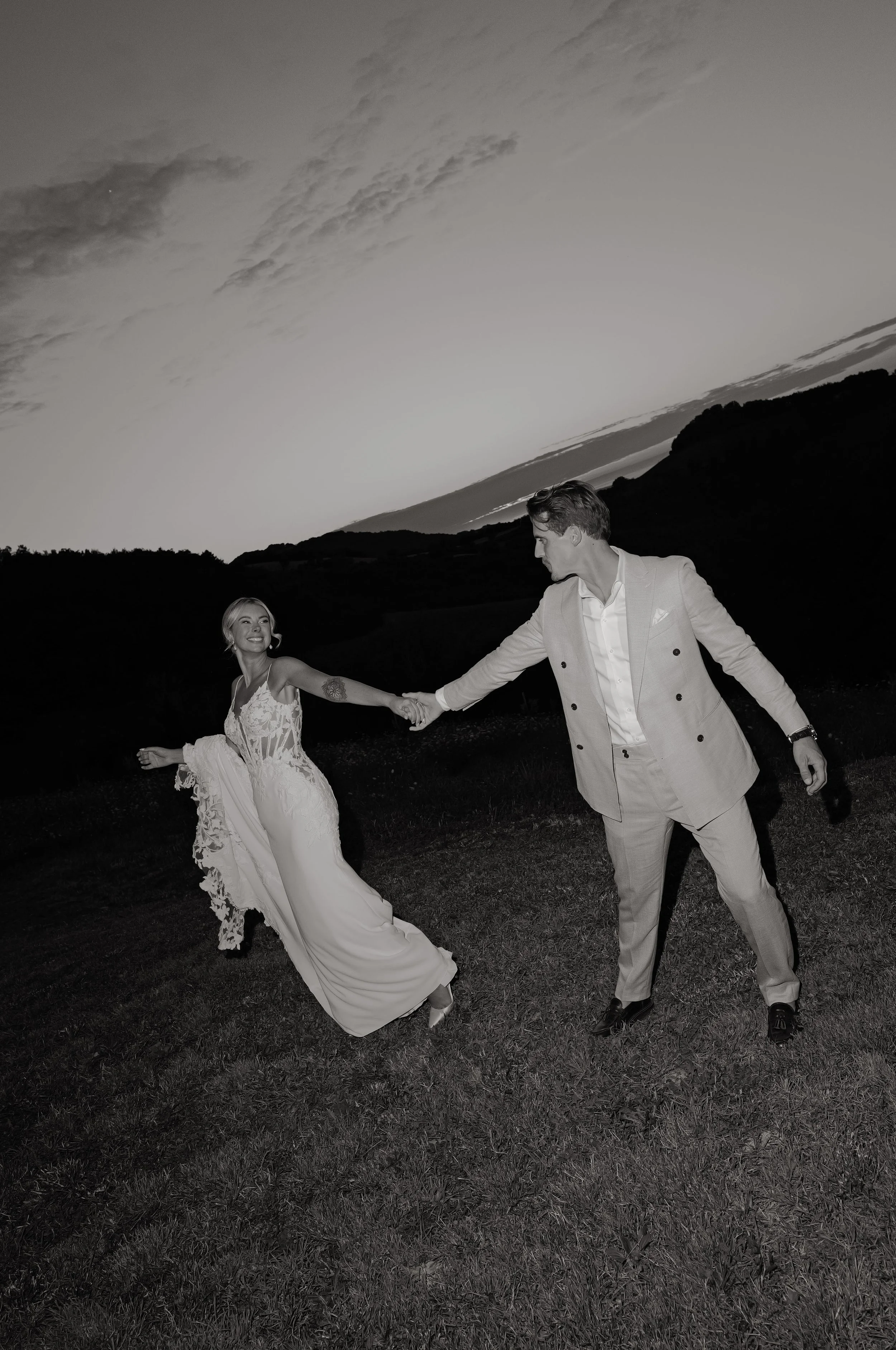 Una coppia in abiti da sposa e sposo tiene mano e danza su un prato all'aperto al tramonto.