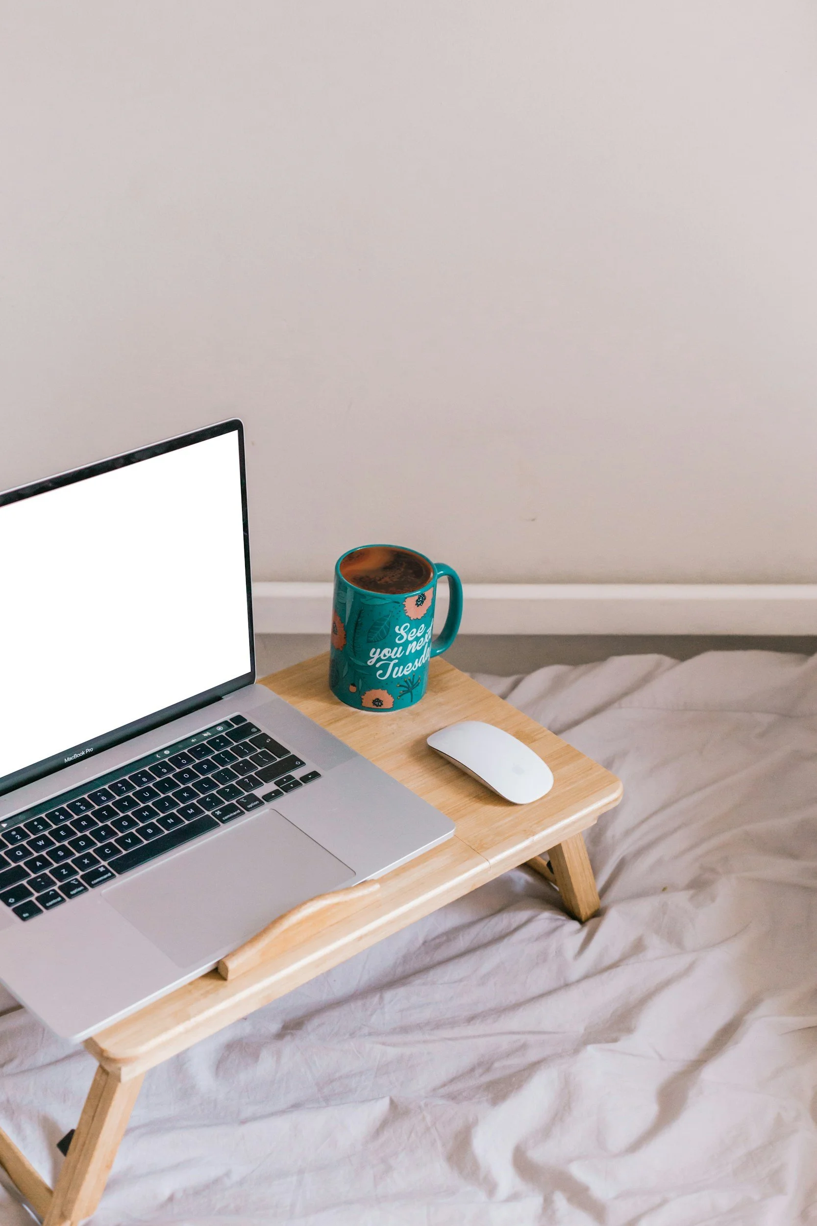 Laptop, white mouse, turquoise coffee mug with a floral design, and text on the mug that says "See you next Tuesday" on a wooden table symbolizing the telehealth option and benefit of doing therapy from home.