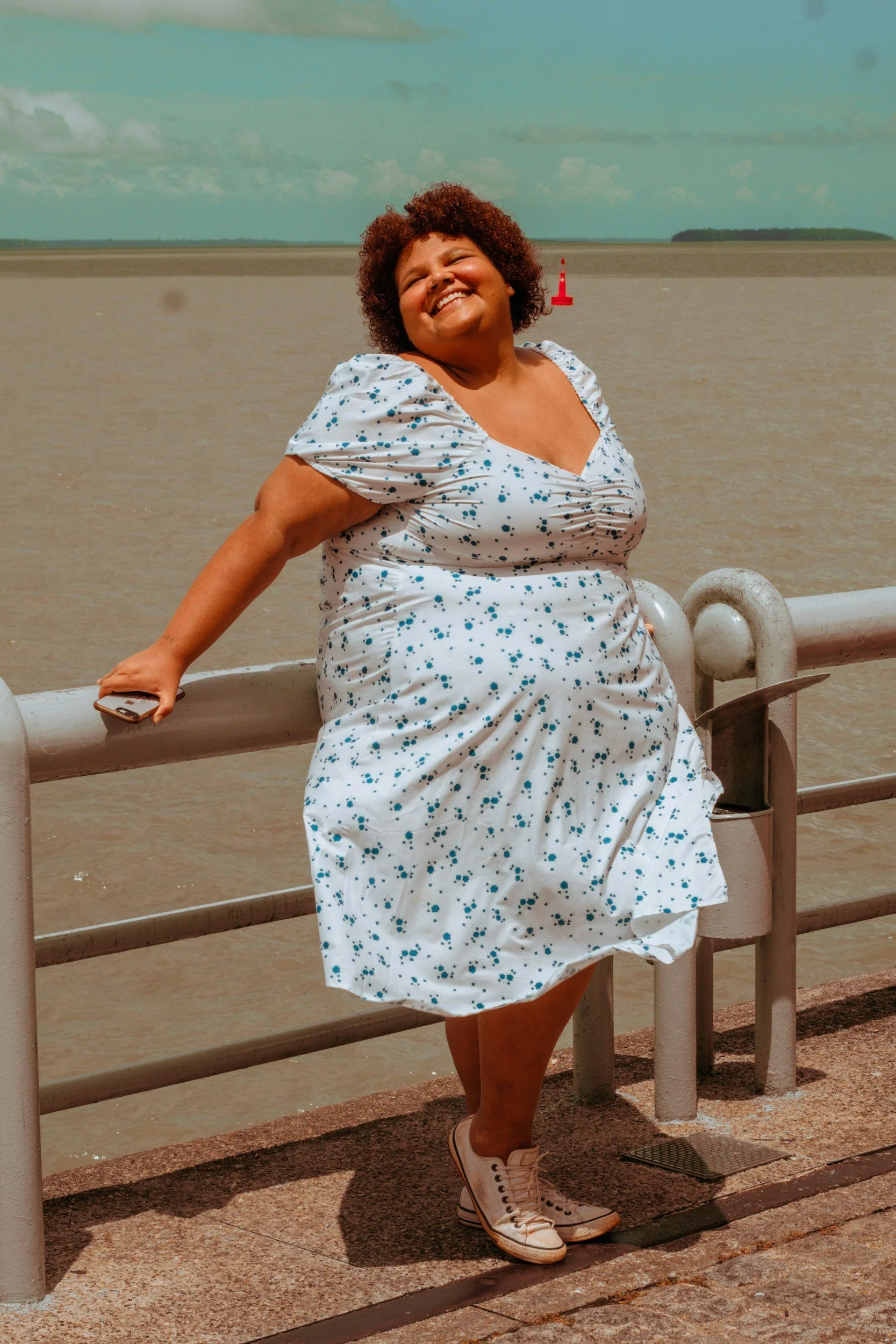 Smiling woman in a white dress with blue splatter pattern, white sneakers, and curly hair, feeling hopeful representing the trauma informed therapy provided at Cove Counseling Group