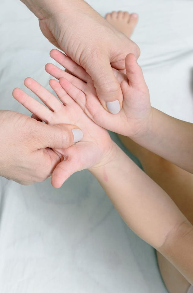 Adult hands gently holding and stretching a child's open hand, focusing on hand care or massage.