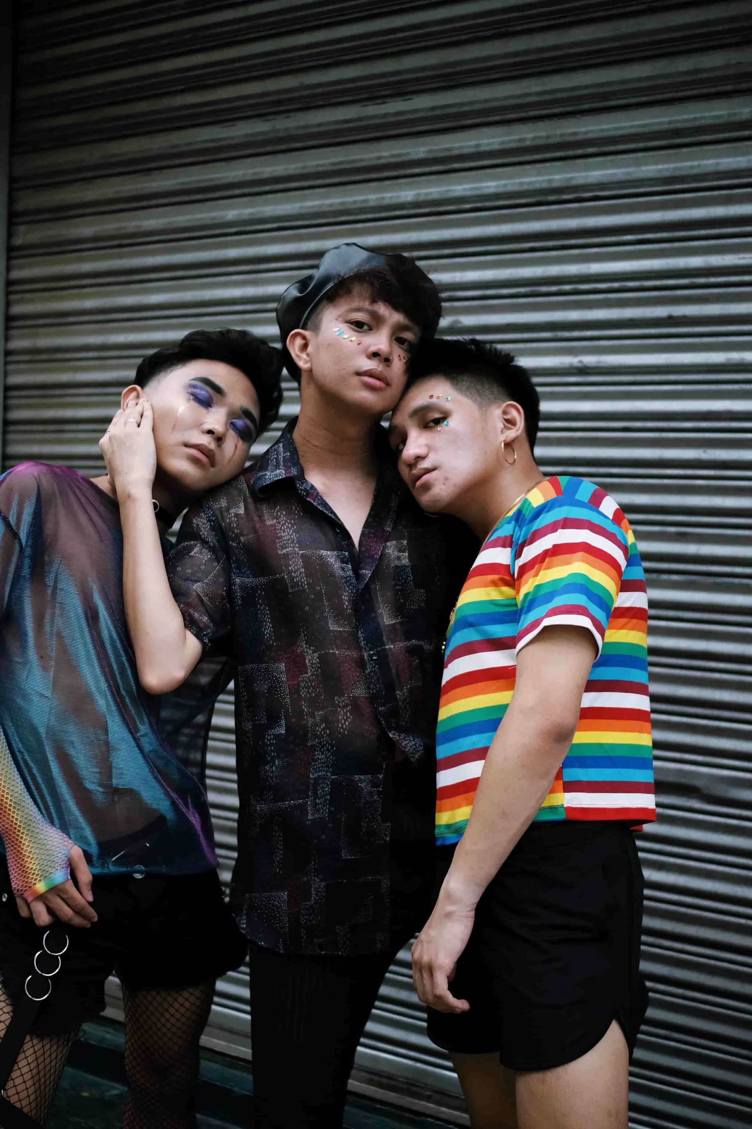 Three people posing together in front of a closed metal shutter, wearing colorful and patterned clothing.
