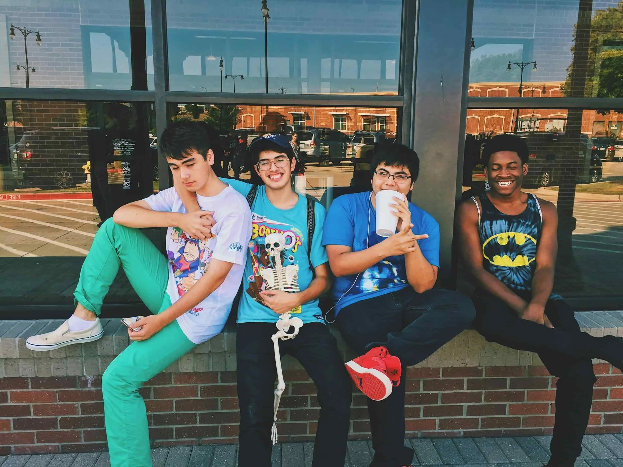 A group of 4 teenage boys sit together enjoying a nice summer day outside in front of a store