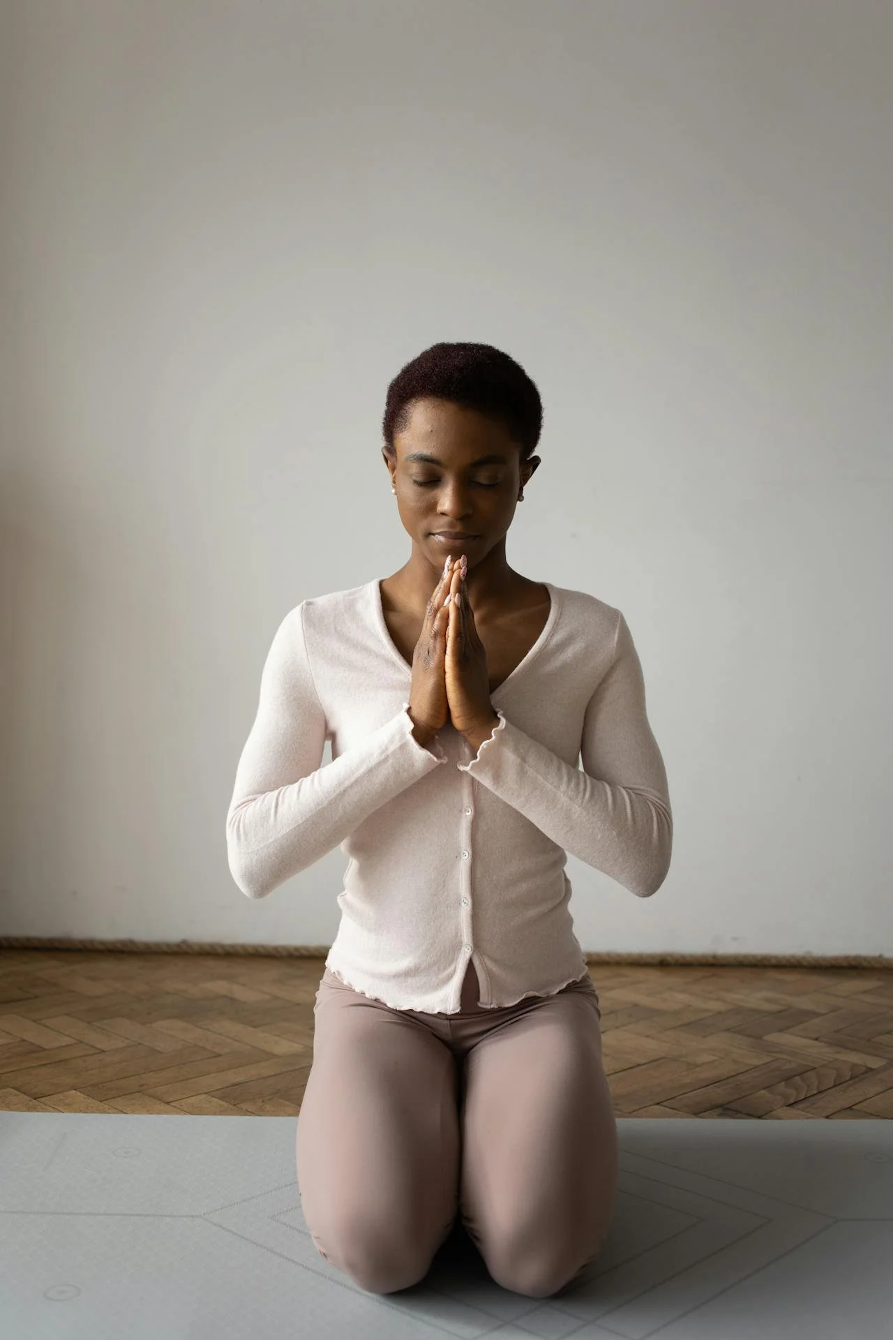 A woman kneels with her eyes closed and palms together at her chest in namaste