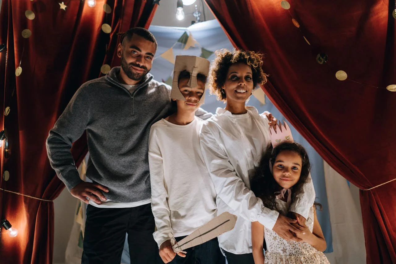 A family of four stands in front of a theater curtain on stage