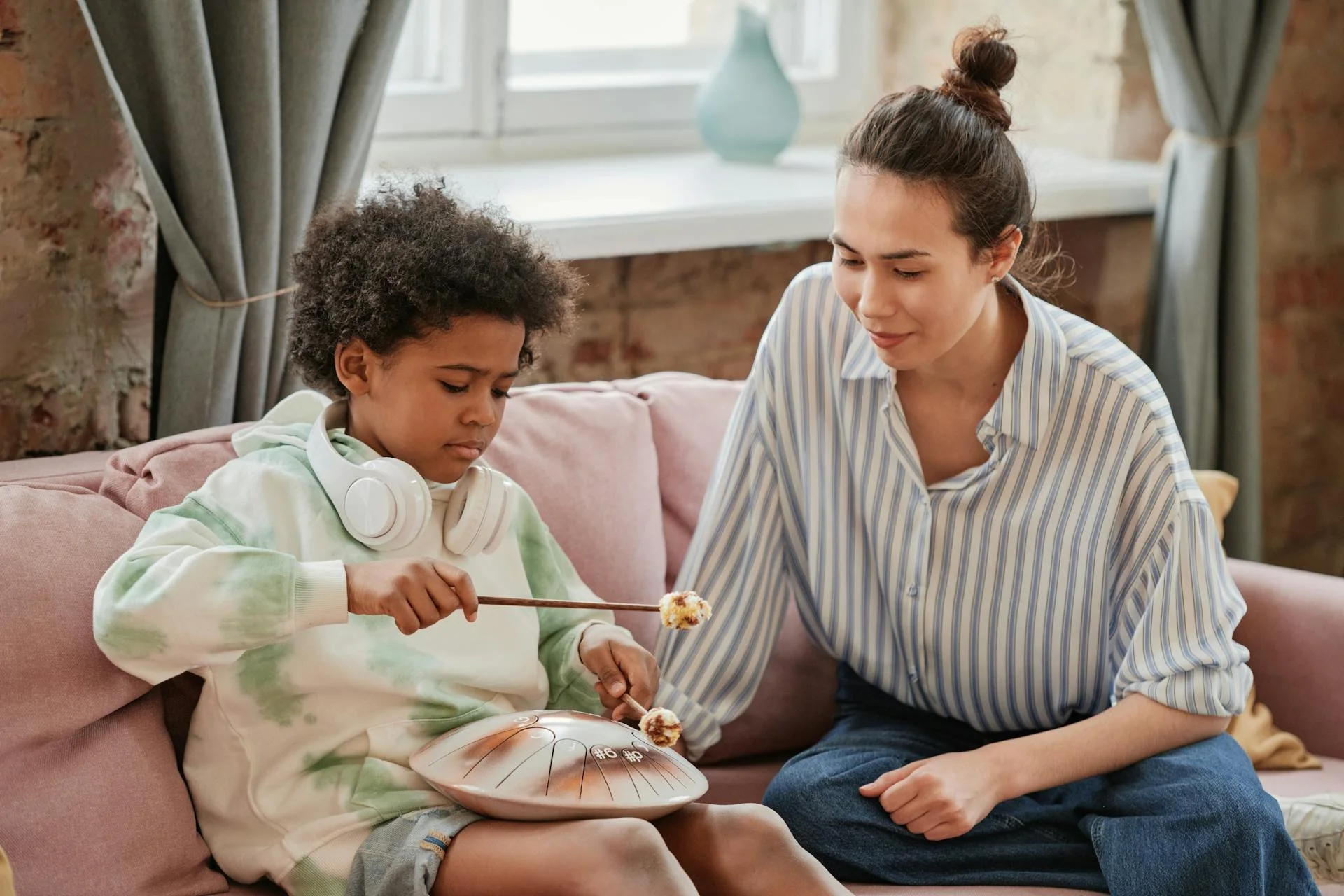 A woman sits with a child on a couch watching him play a musical instrument