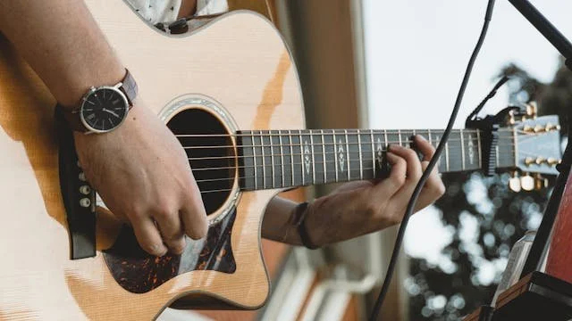 Close-up of a person playing an acoustic guitar, showing hands on the strings and fretboard with a microphone nearby.