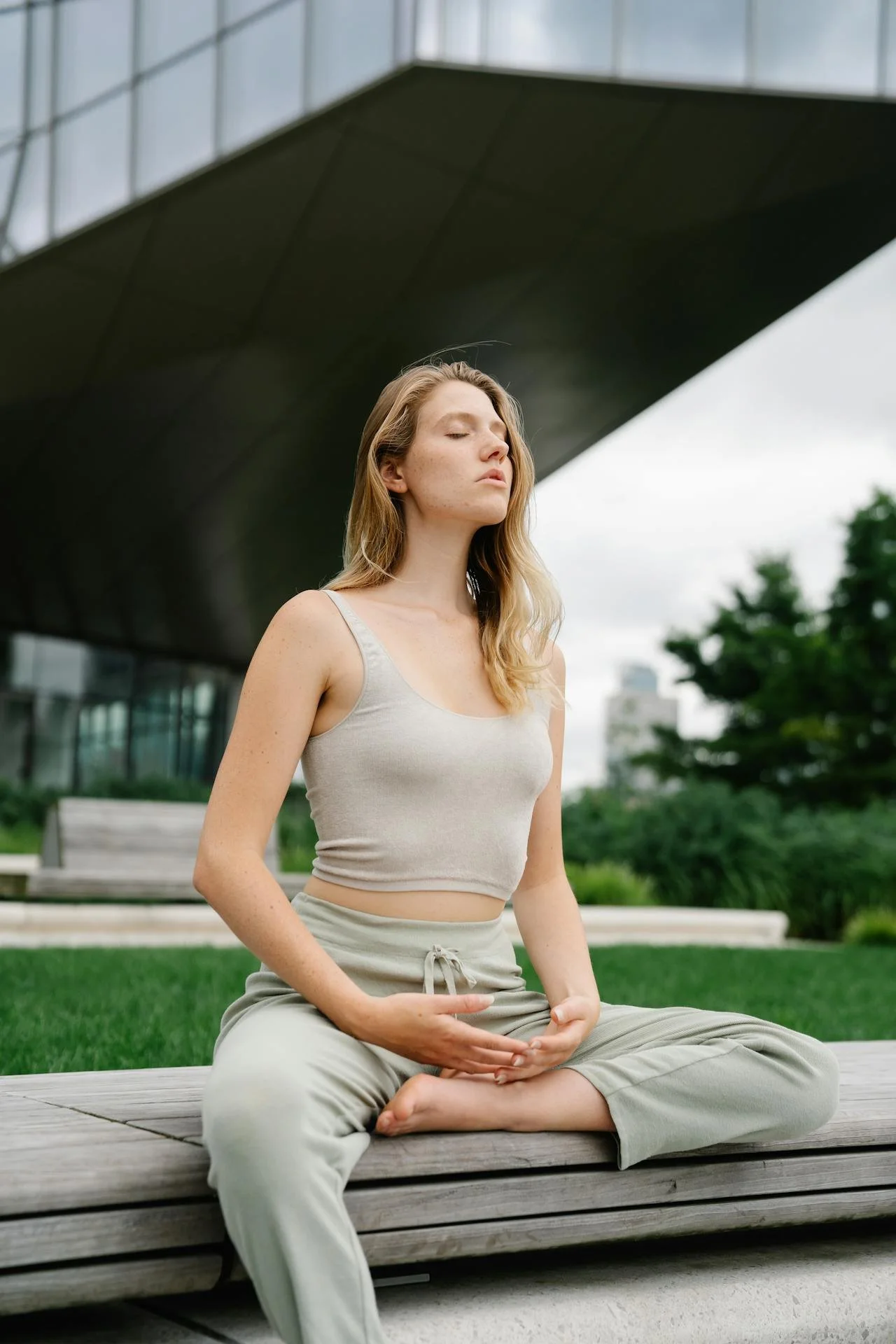 A woman sits outdoors on a bench in a peaceful meditative pose