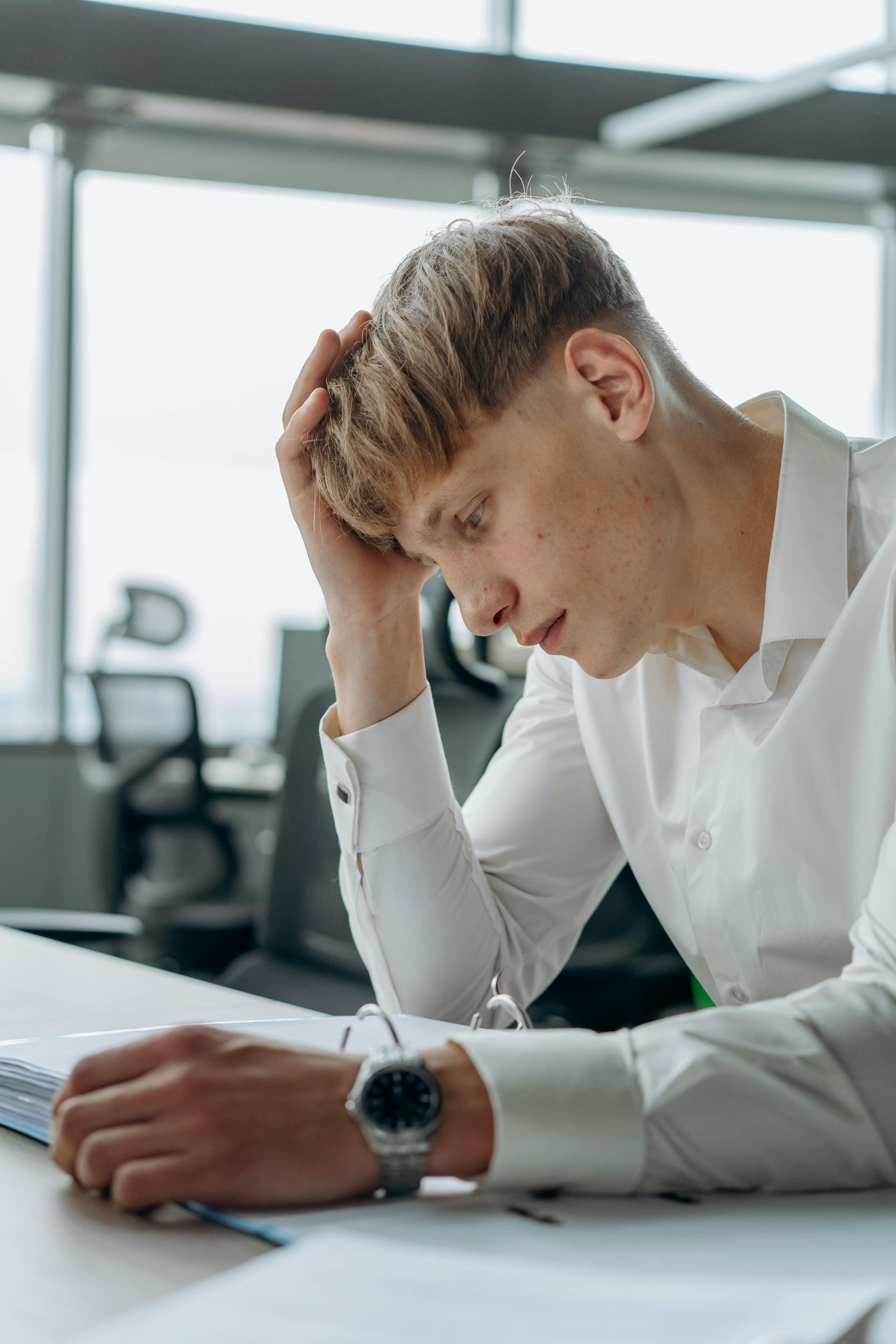 A man sits at his desk with an open notebook holding his head in his hand appearing overwhelmed