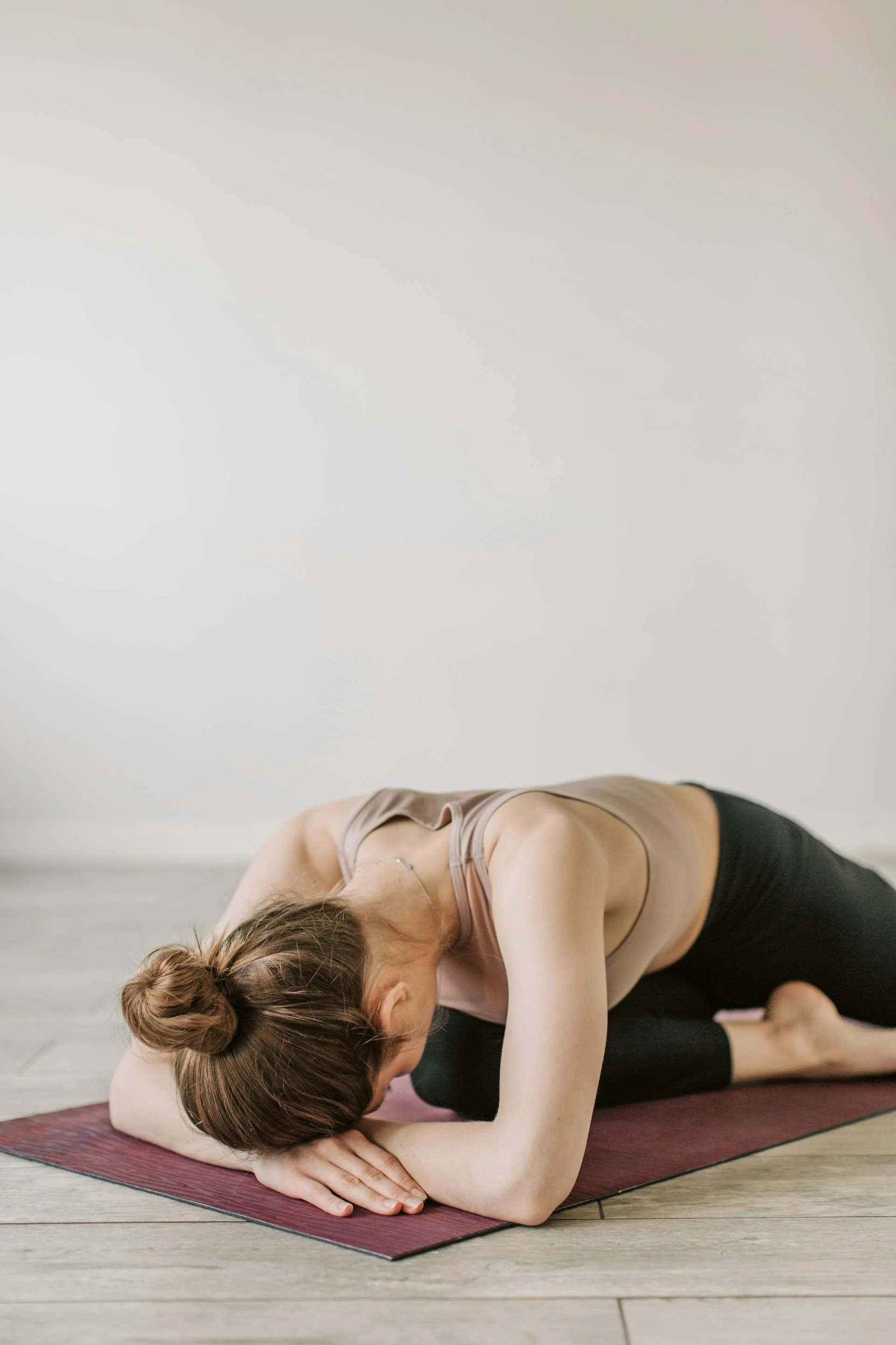 A woman on a yoga mat rests her head on her elbows in front of her in a pose