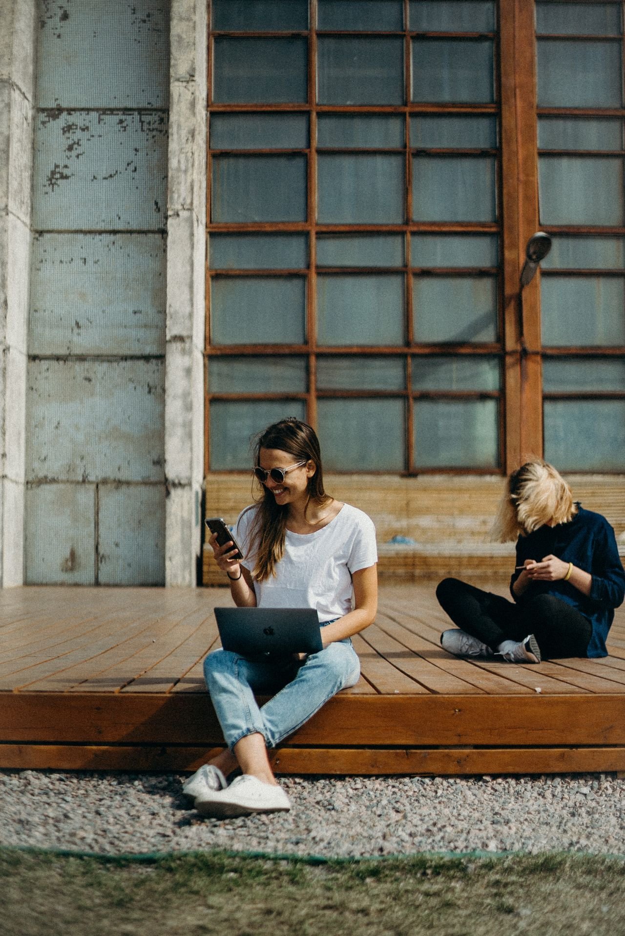 Two people sit outside on a deck happily interacting with others on their electronic devices