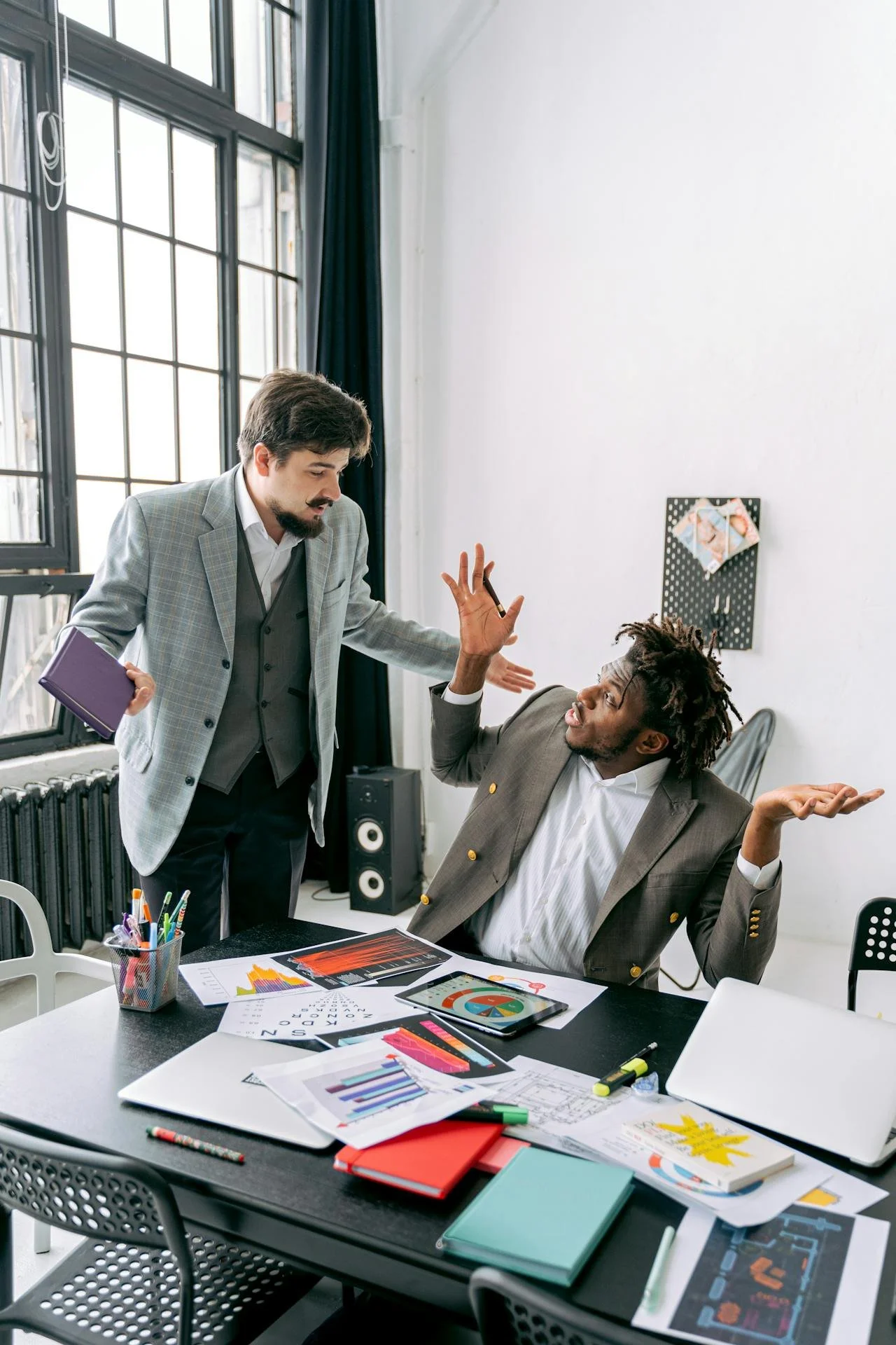 Two people having a heated discussion over charts and documents in a modern office with large windows.