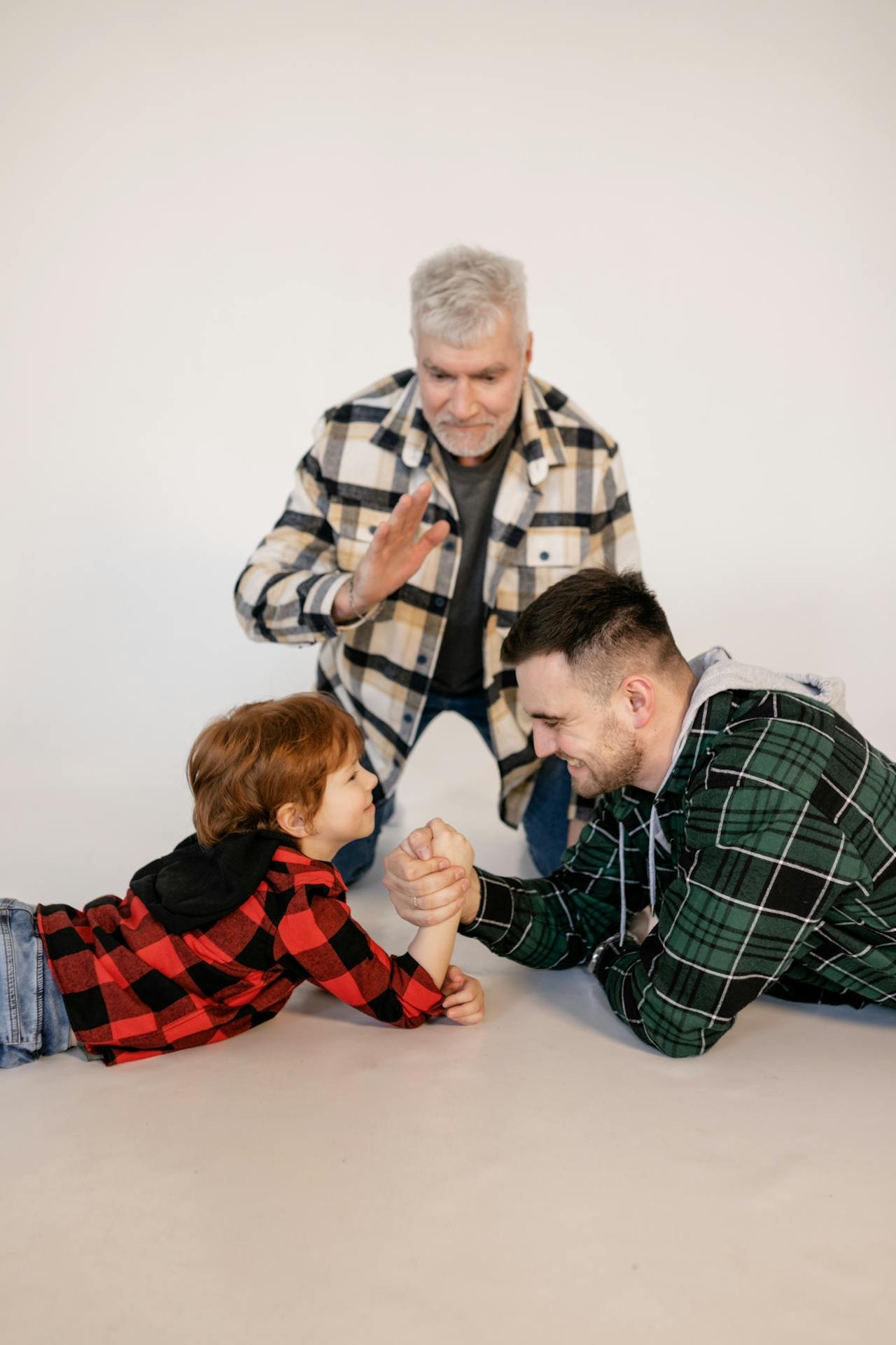 Three people, fathers and sons, of different age generations engage playfully in an arm wrestle.