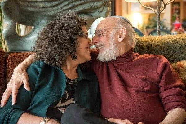 John and Julie Gottman sitting on couch smiling at each other