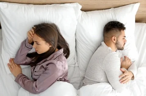 A couple lying in bed with their backs towards each other turning away in distress