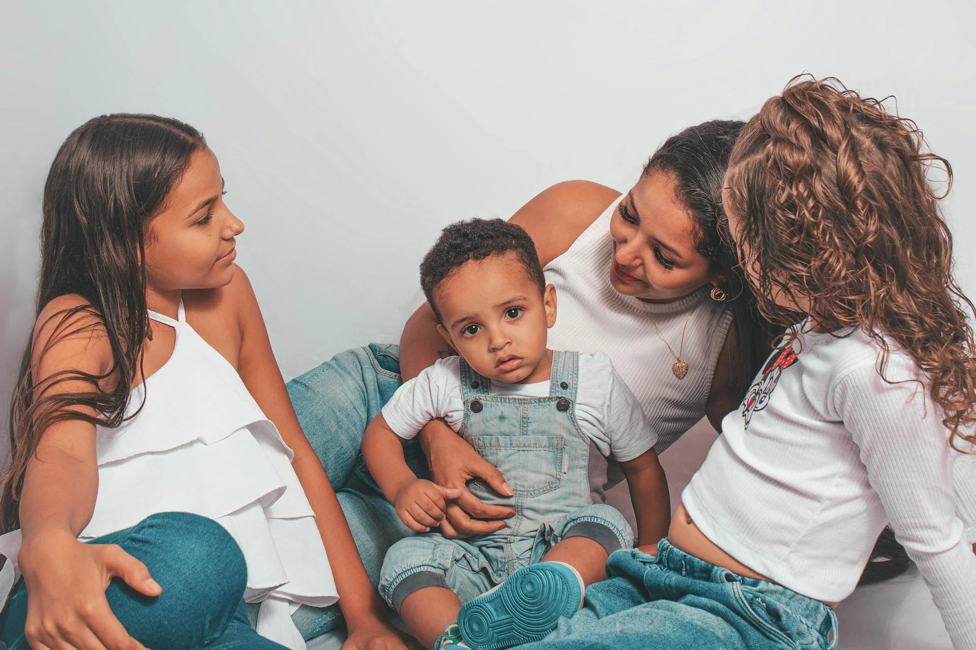 Group of four people sitting together against a plain background, three girls in white tops and one boy in denim overalls.