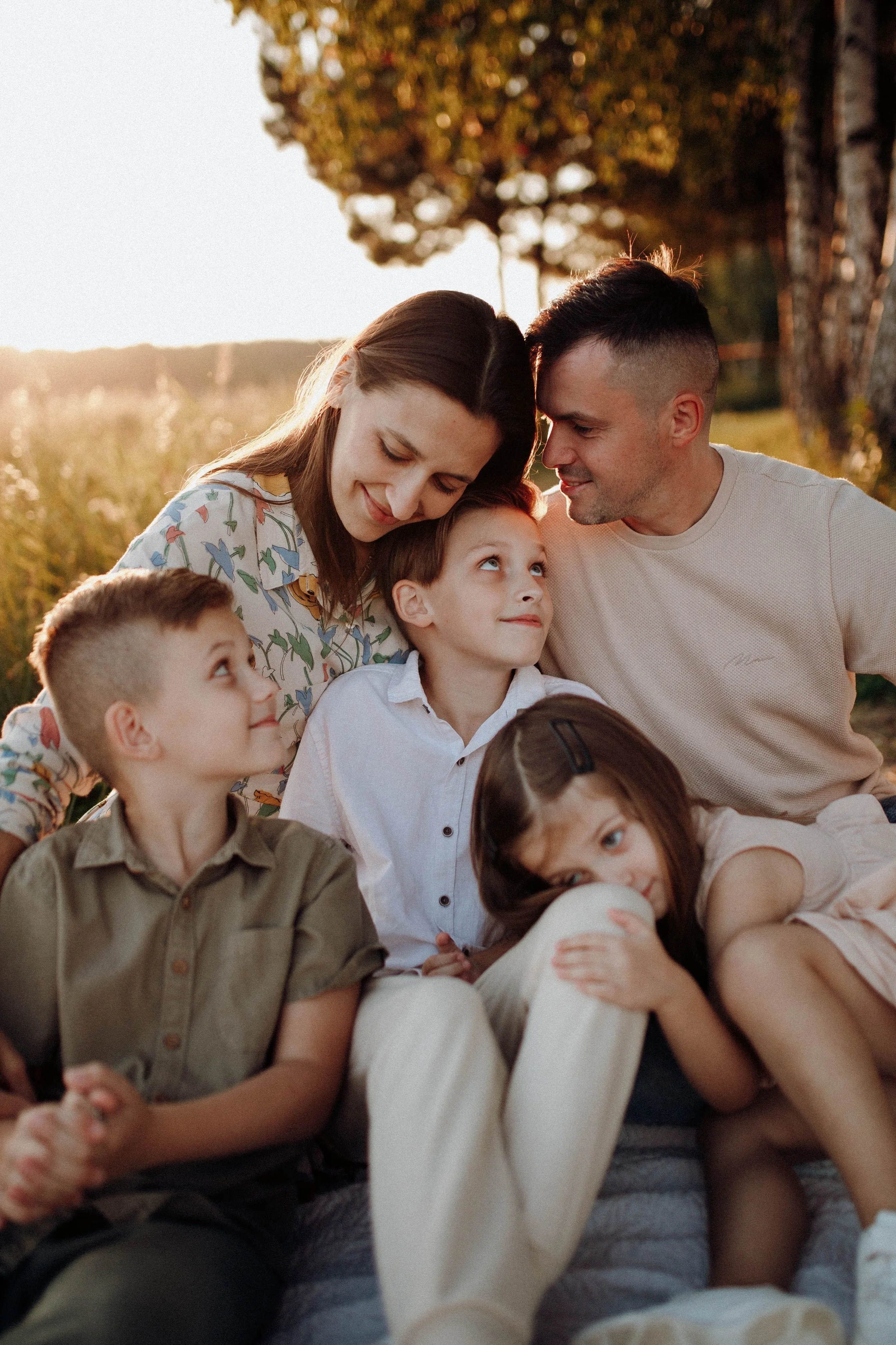A family of six people sitting outside in a park during sunset, smiling and enjoying each other's company.