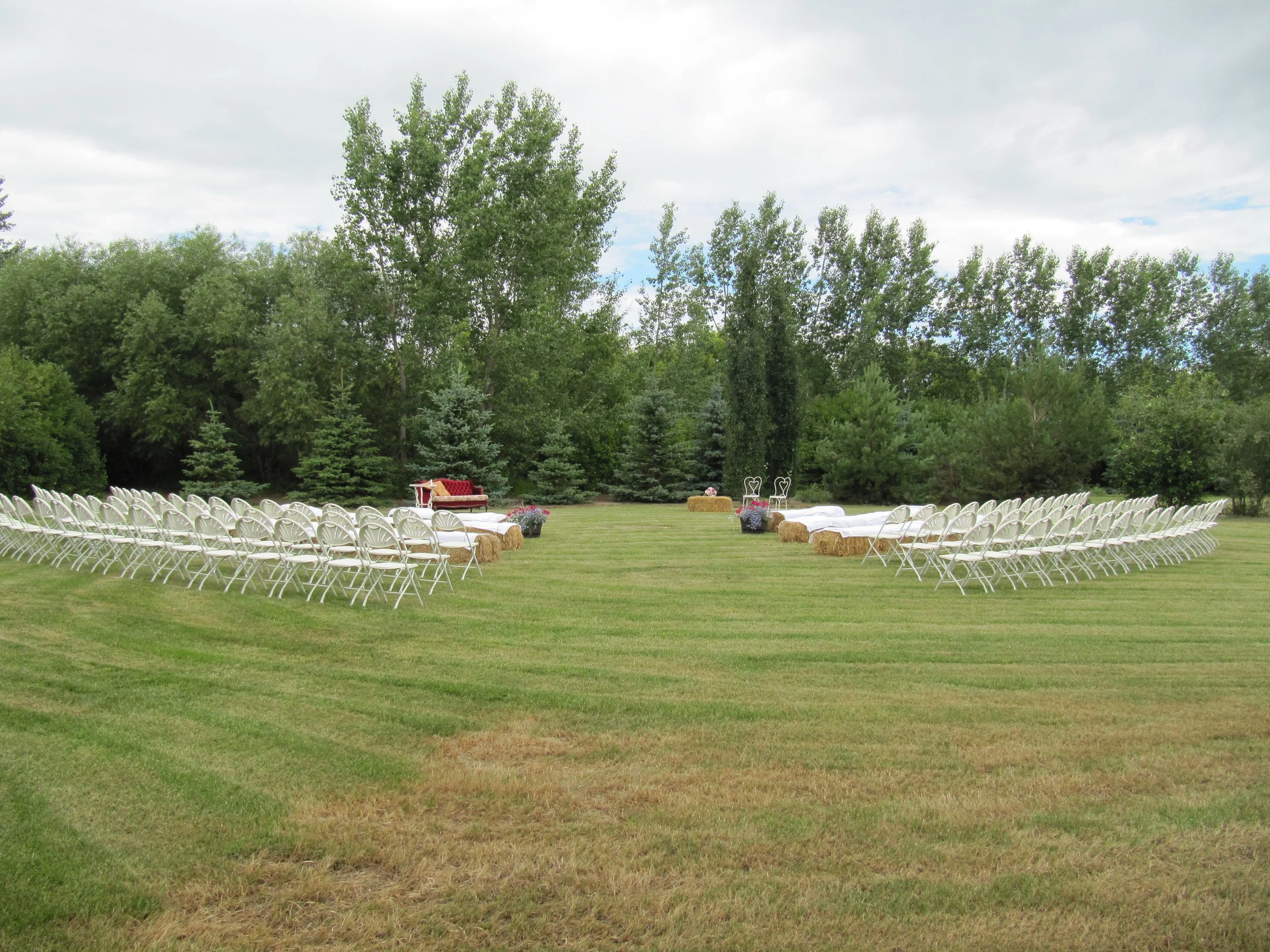 Outdoor ceremony and reception area with white chairs and natural prairie scenery.