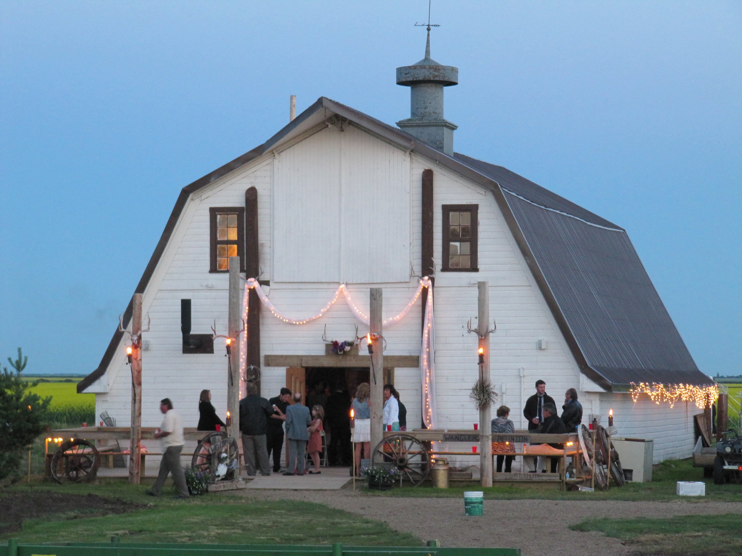 Front of the wedding barn with guests on the patio beneath string lights.