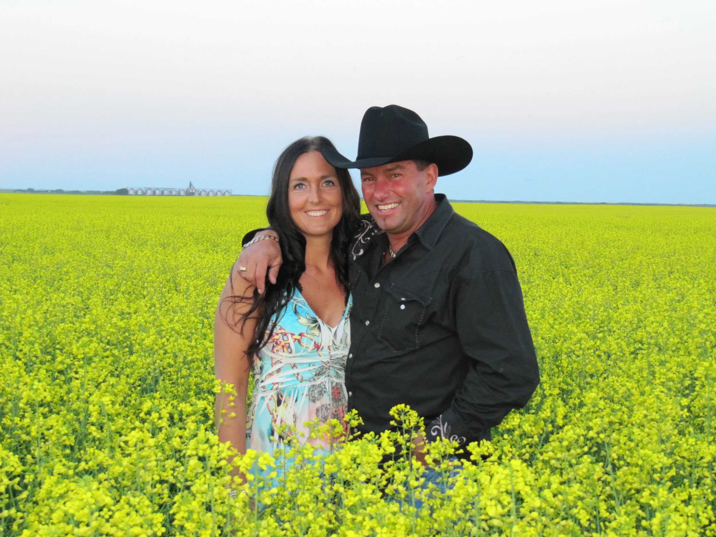 Owners  of Top Gun Saloon standing in a vibrant Saskatchewan canola field, celebrating the beauty of praire life