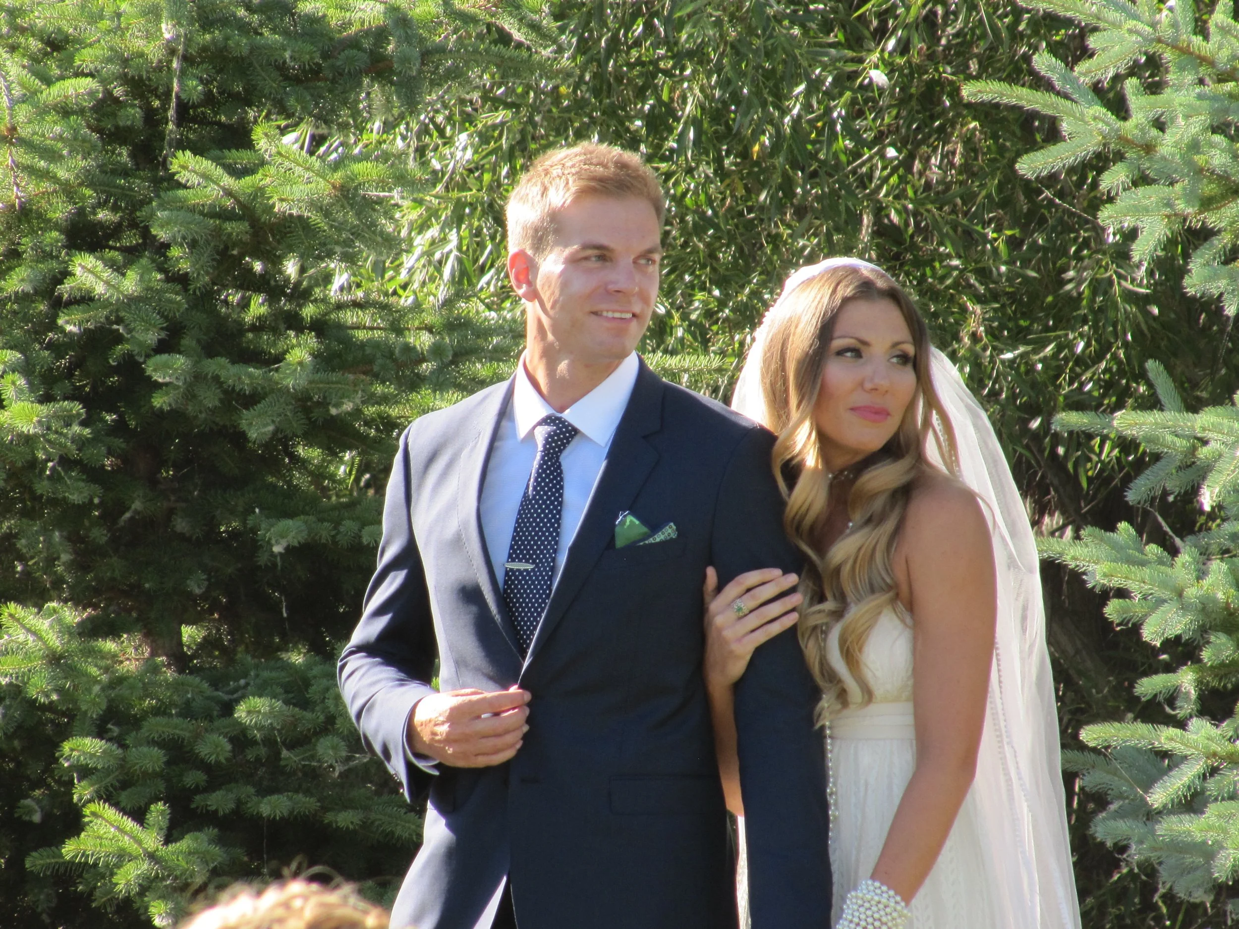 Close up portrait of the bride and groom with green trees in background.