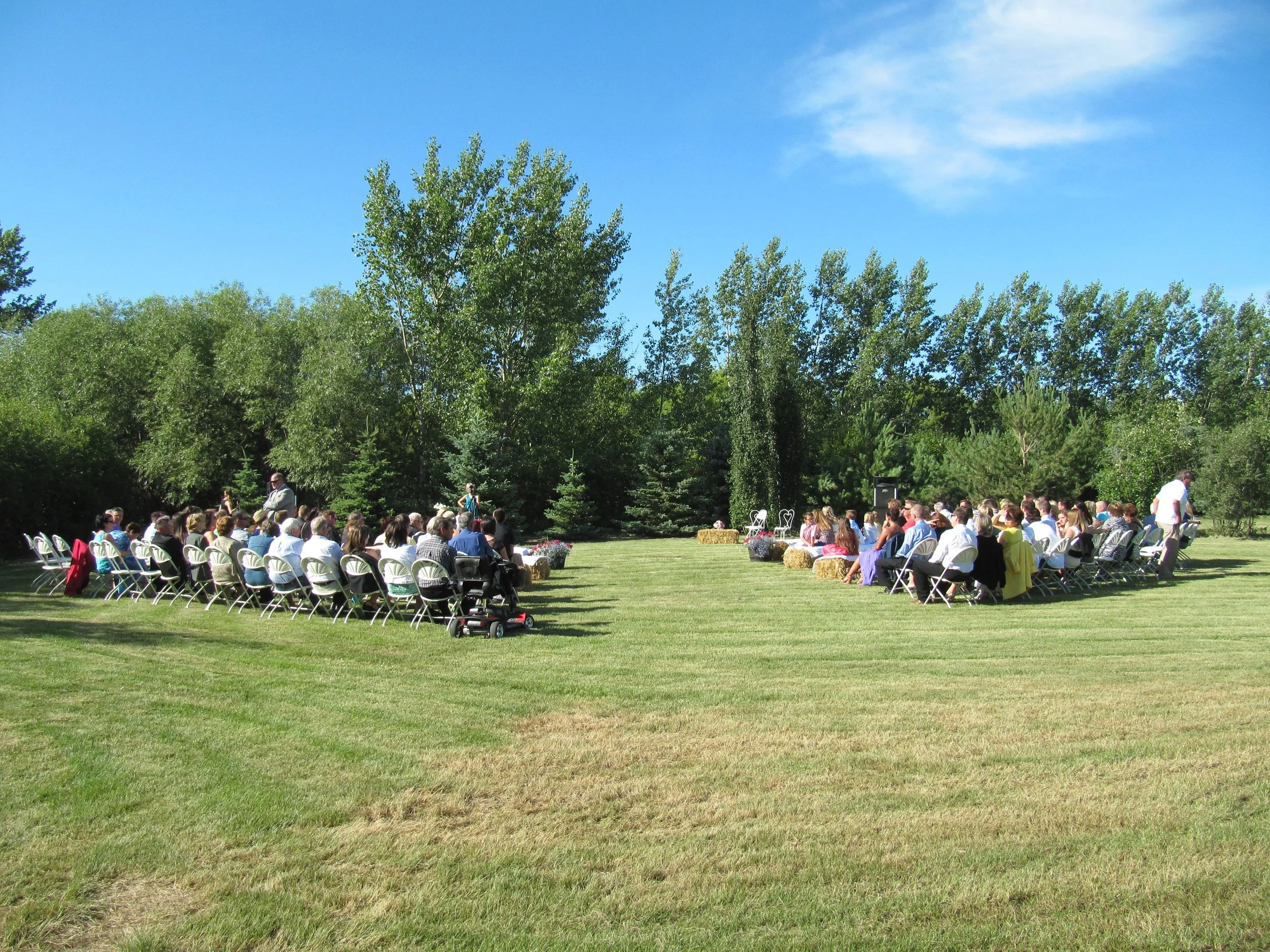 Outdoor wedding reception with guests seated on green grass beneath blue skies