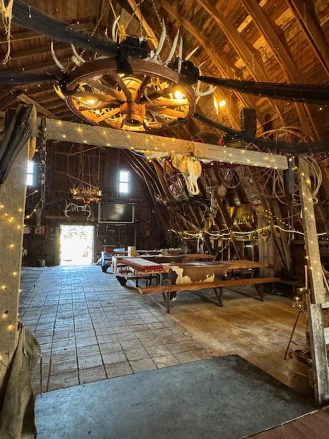 Rustic barn interior featuring wagon wheels, western decor, and string lighting.
