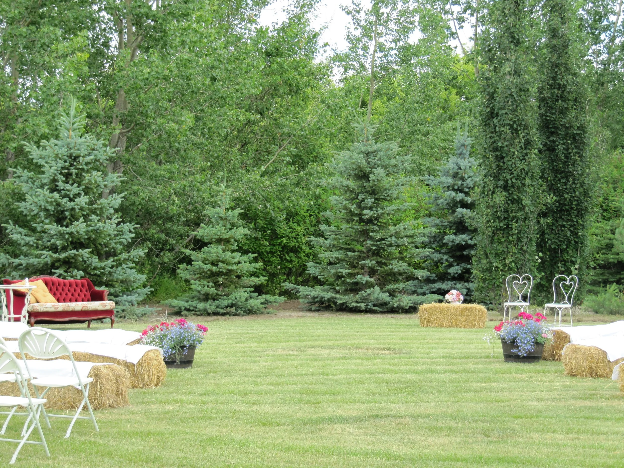 Rustic reception area featuring  a vintage red couch, hay bale seating and ceremony chairs.