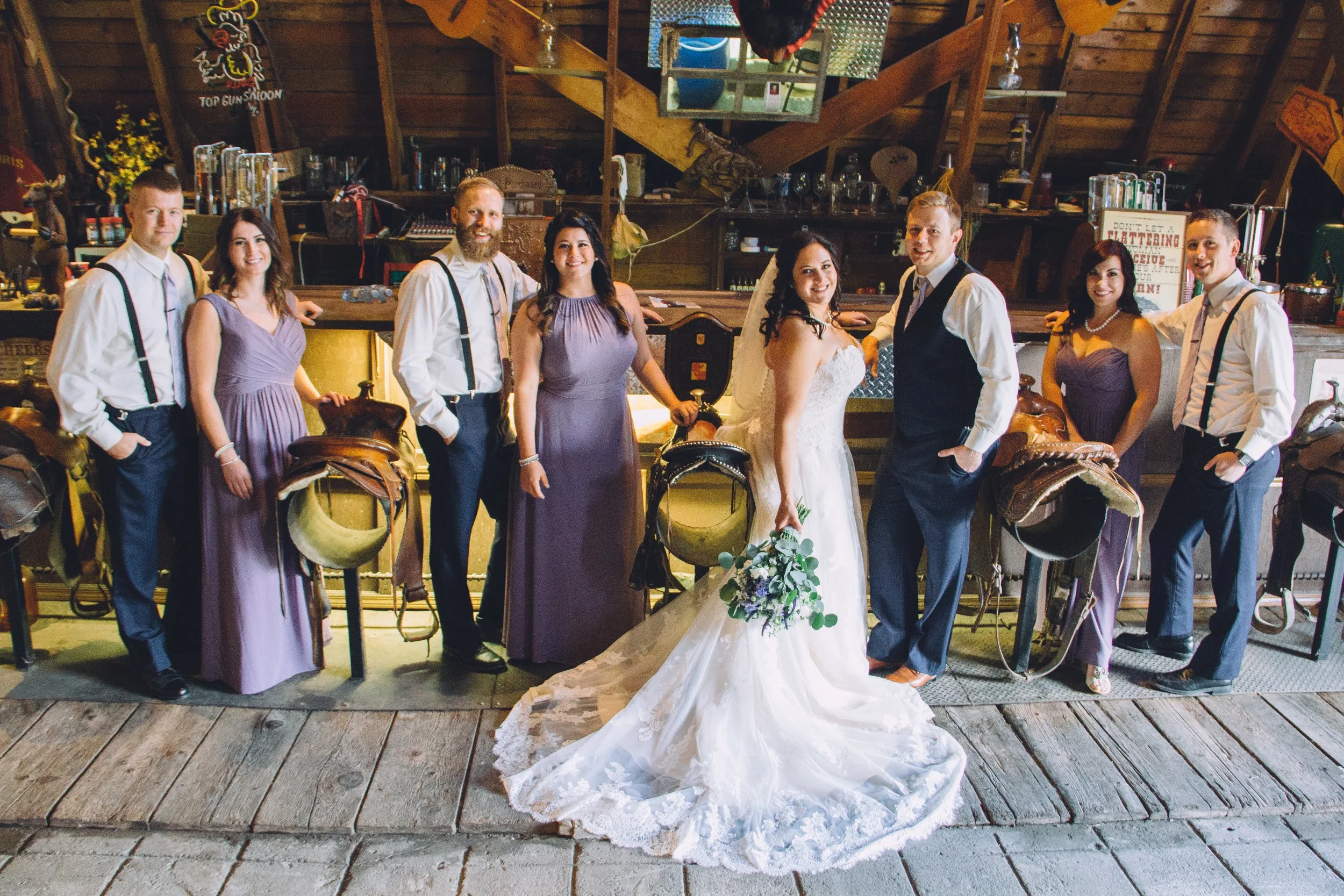Bride and groom with their wedding party gathered in front of the rustic bar and saddle barstools