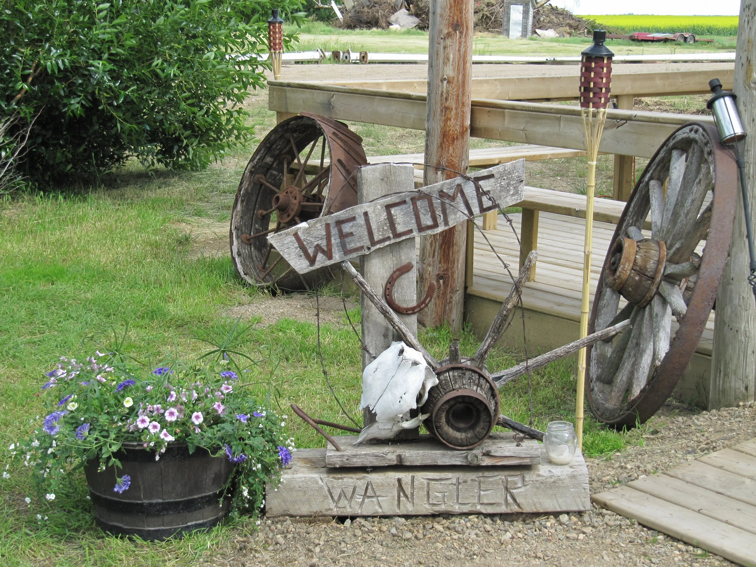 Rustic welcome sign with antique wagon wheel and colourful flowers at the entrance to Top Gun Saloon