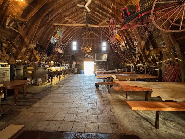 Handmade picnic tables beneath a suspended vintage wagon in side the barn.