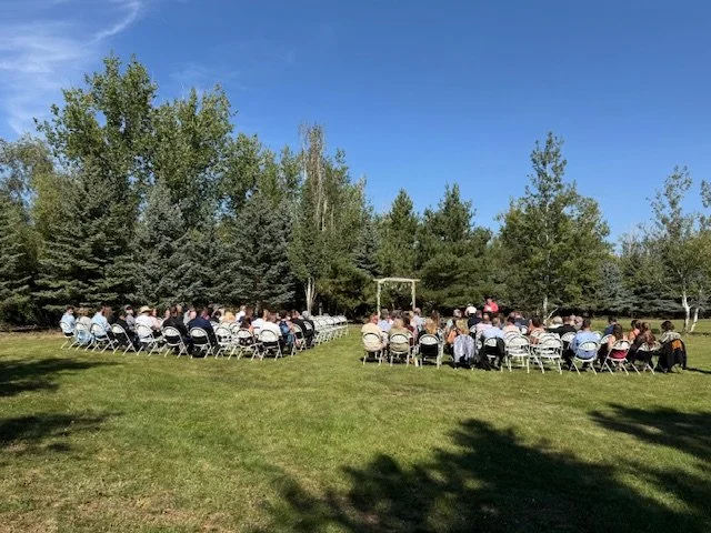 Wide view of wedding guests seated outdoors during the ceremony beneath blue skies.