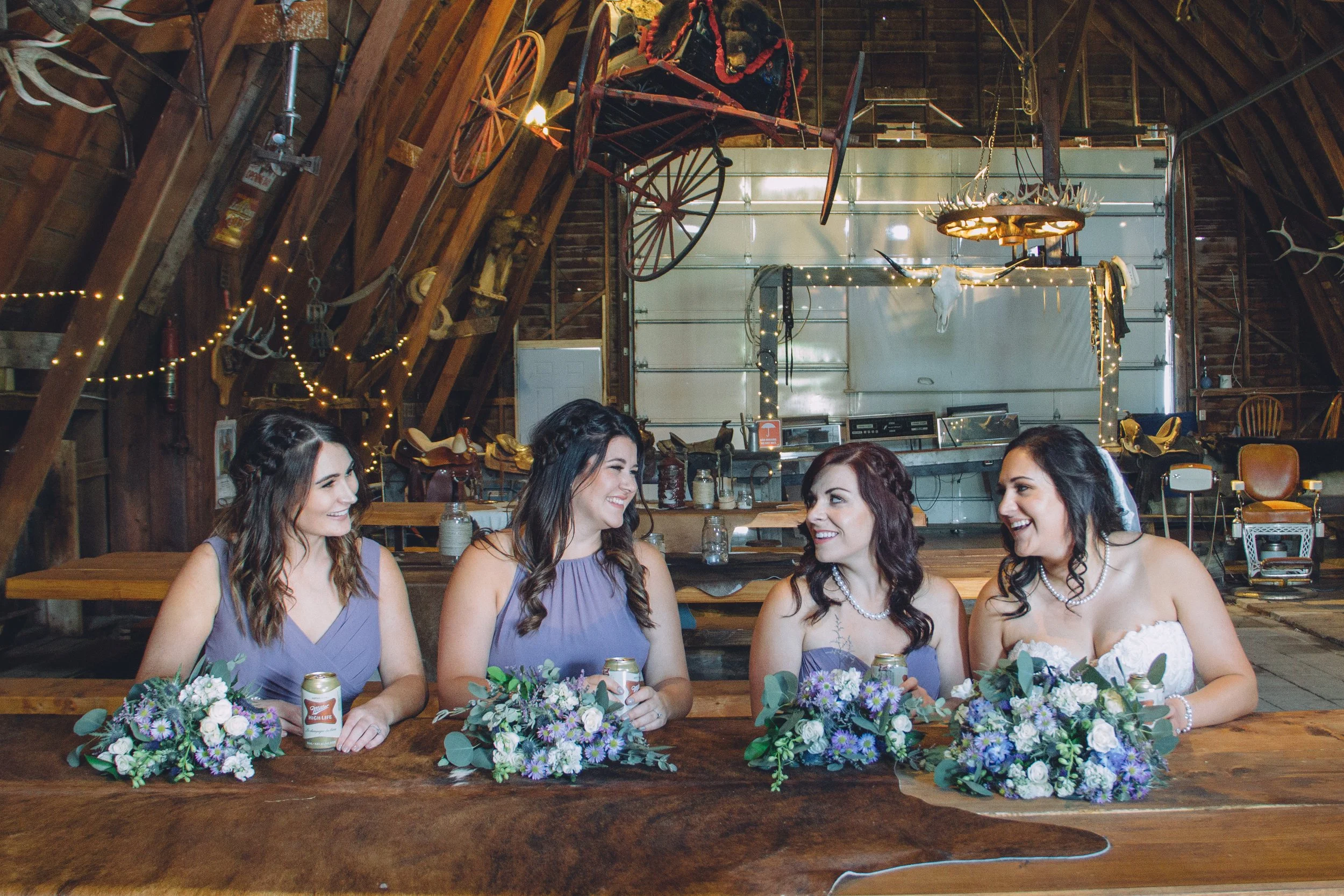 Four bridesmaids in lavender dresses holding bouquets while seated at the handmade picnic table