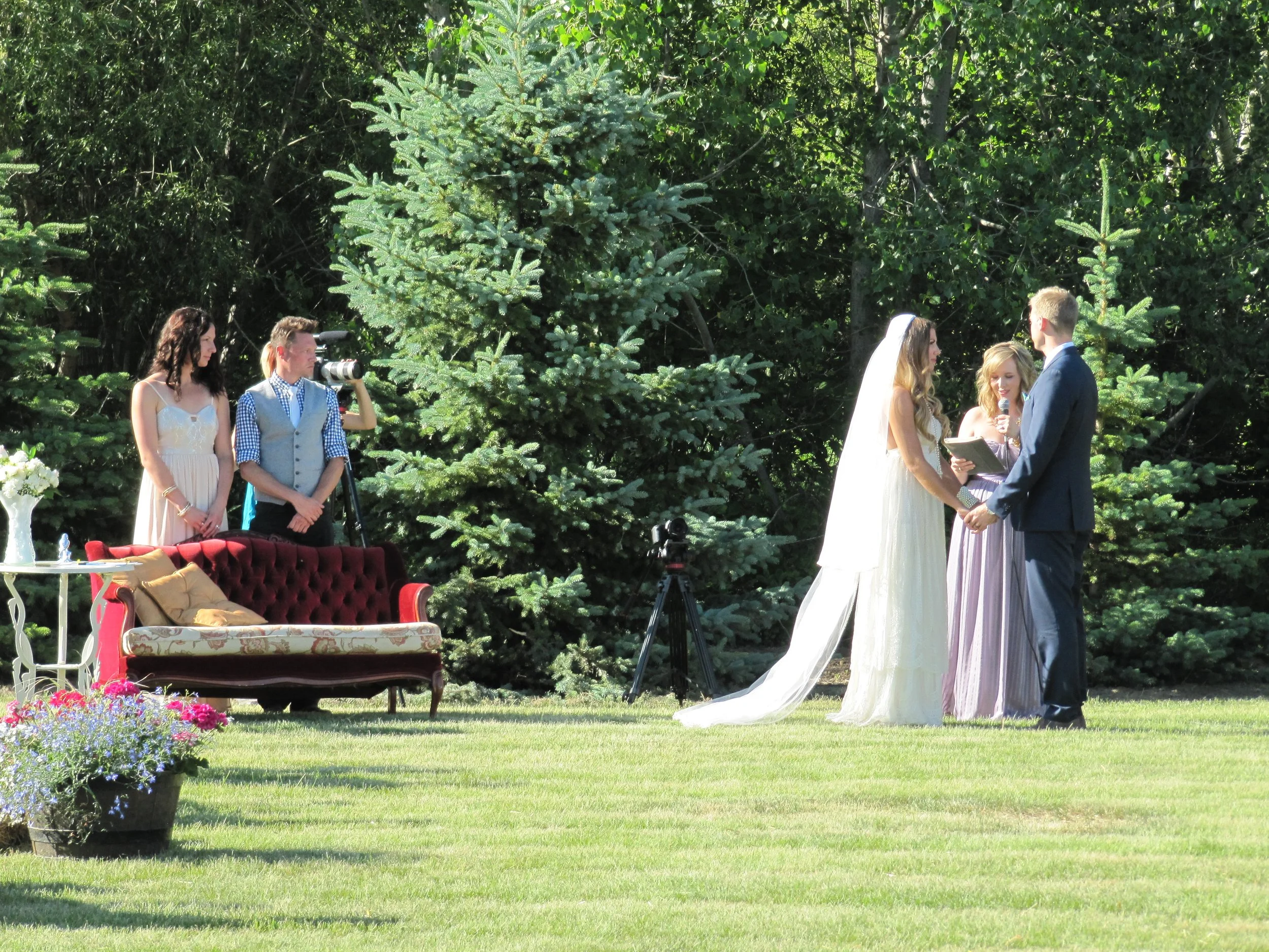 Bride and groom exchanging vows beside a vintage red couch during their ceremony.