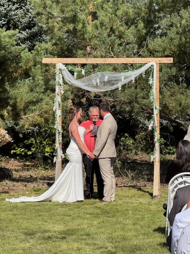 Bride and groom exchanging vows beneath handmade wooden ceremony arch.