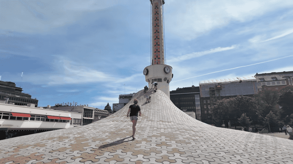 Visitors walking and climbing on the curved Amos Rex rooftop installation with the Lasipalatsi tower in the background.