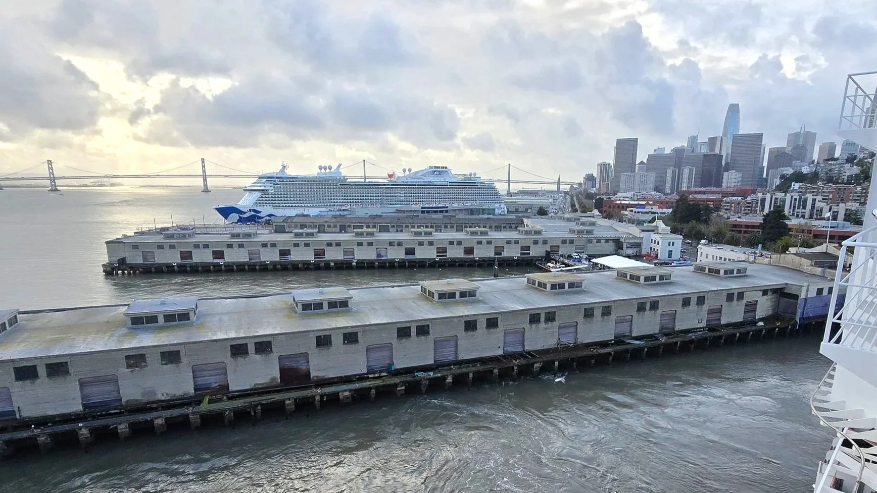 San Francisco Cruise Port at Pier 27 with a cruise ship docked near the Embarcadero, Bay Bridge, and downtown skyline on a cloudy day