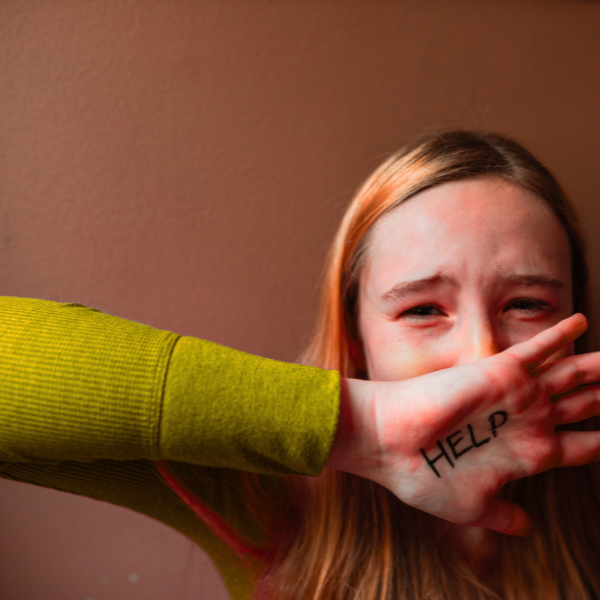 Trauma and Panic - a young girl with long hair appears distressed as a person covers her mouth with their hand, which has the word 'HELP' written on it.trauma counselling Melbourne