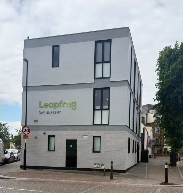 A four-story commercial building with a sign that reads 'Leapfrog Day Nursery' on a city street.
