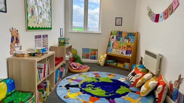 Children's playroom with bookshelves, colorful books, plush toys, a world map rug, and decorated walls.