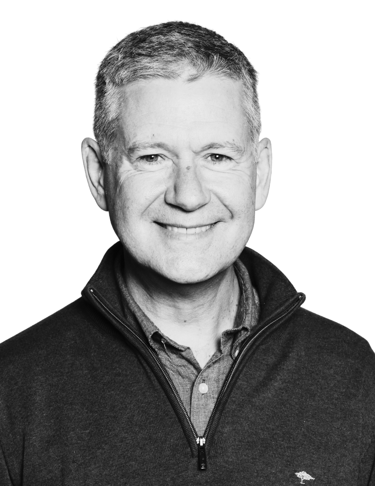 Black and white portrait of a smiling man with short hair, wearing a zip-up jacket and a collared shirt underneath.