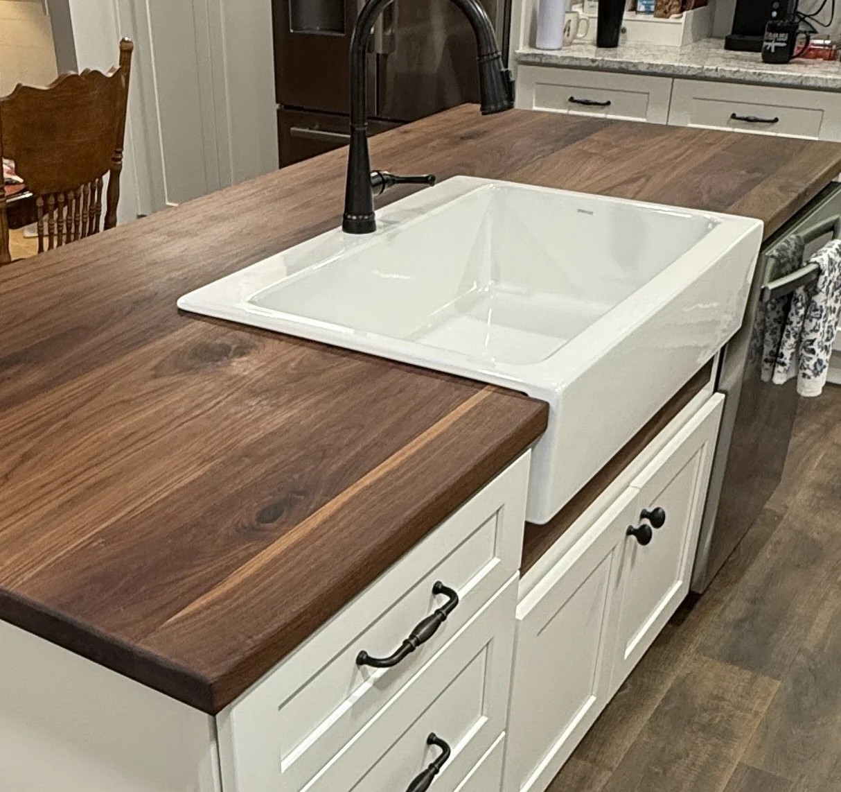 Kitchen island with a farmhouse sink and black gooseneck faucet, wooden countertop, white cabinetry, and a dish towel hanging on the side.