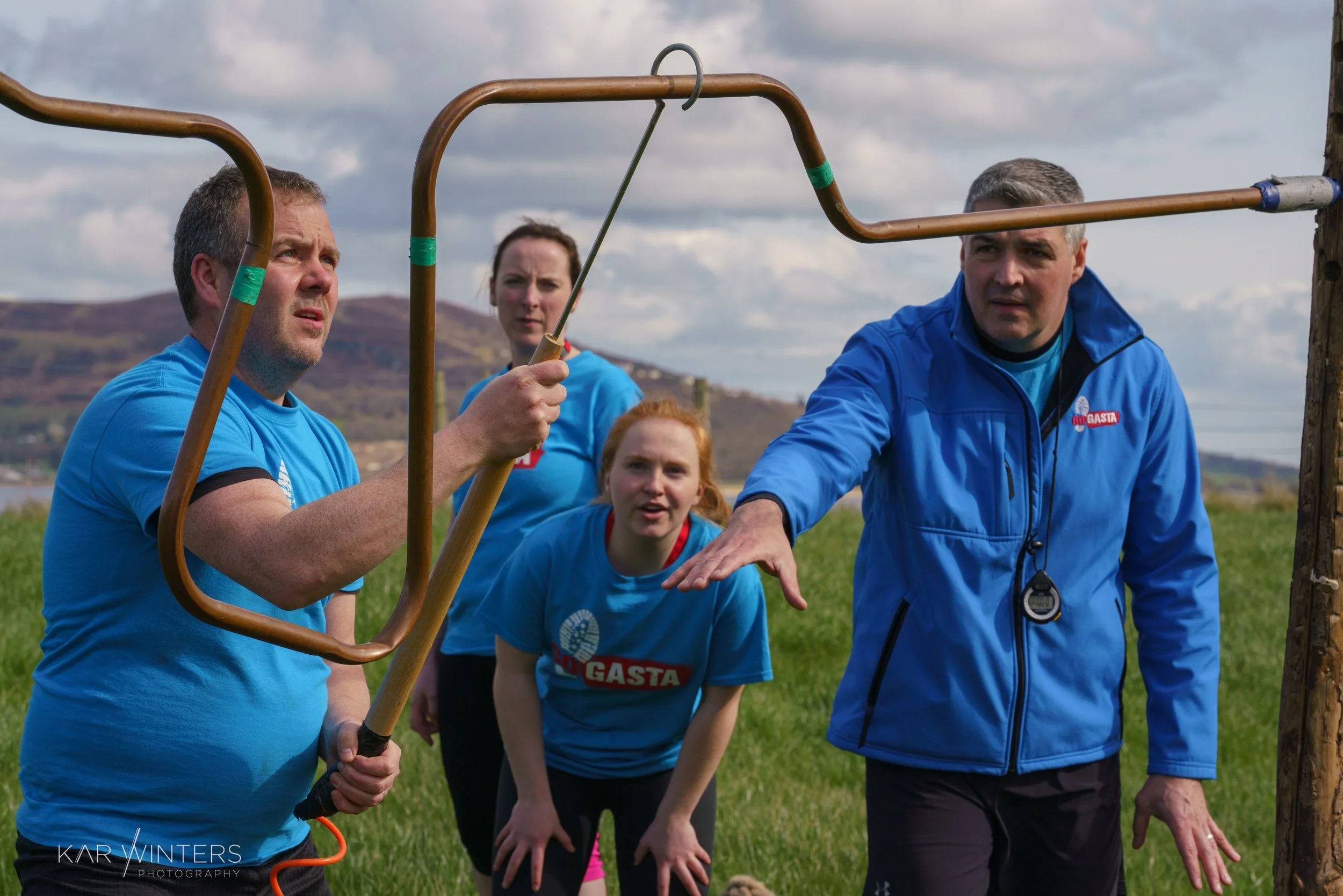 Group of four people outdoors participating in a fence rescue or training, with hills and cloudy sky in the background.