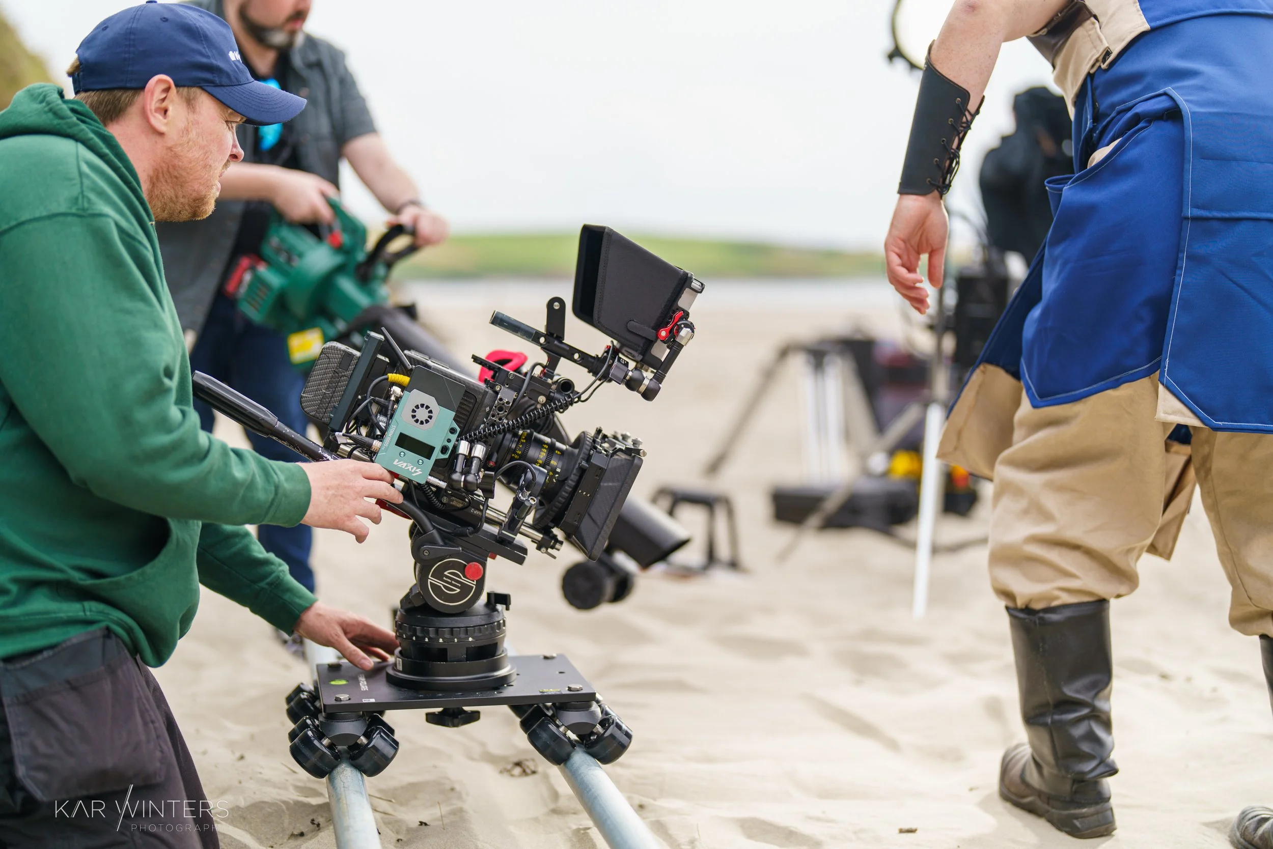Filmmakers preparing a professional camera on a tripod on a beach for a shoot.