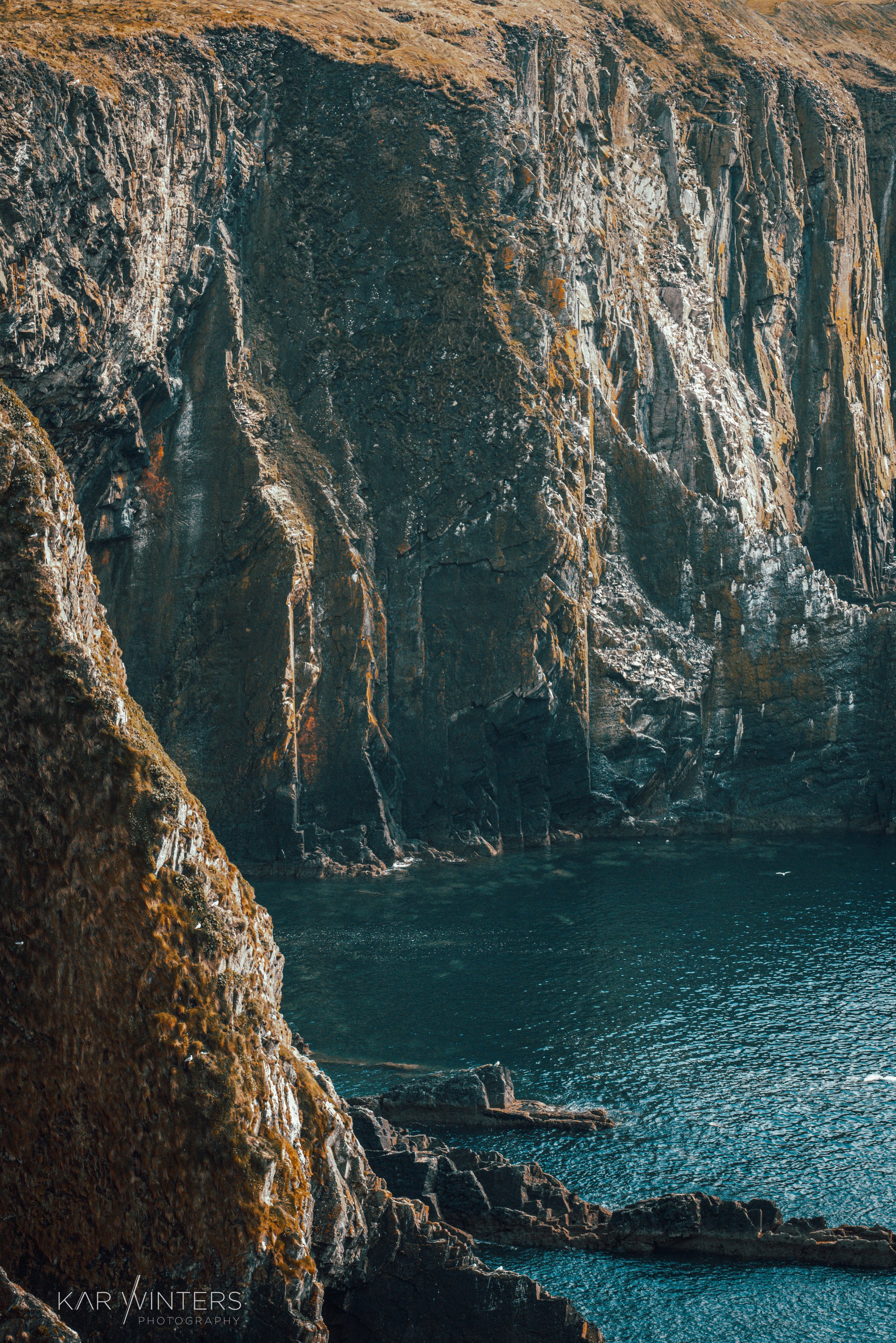 Cliffside overlooking the ocean with steep rock faces and water below.