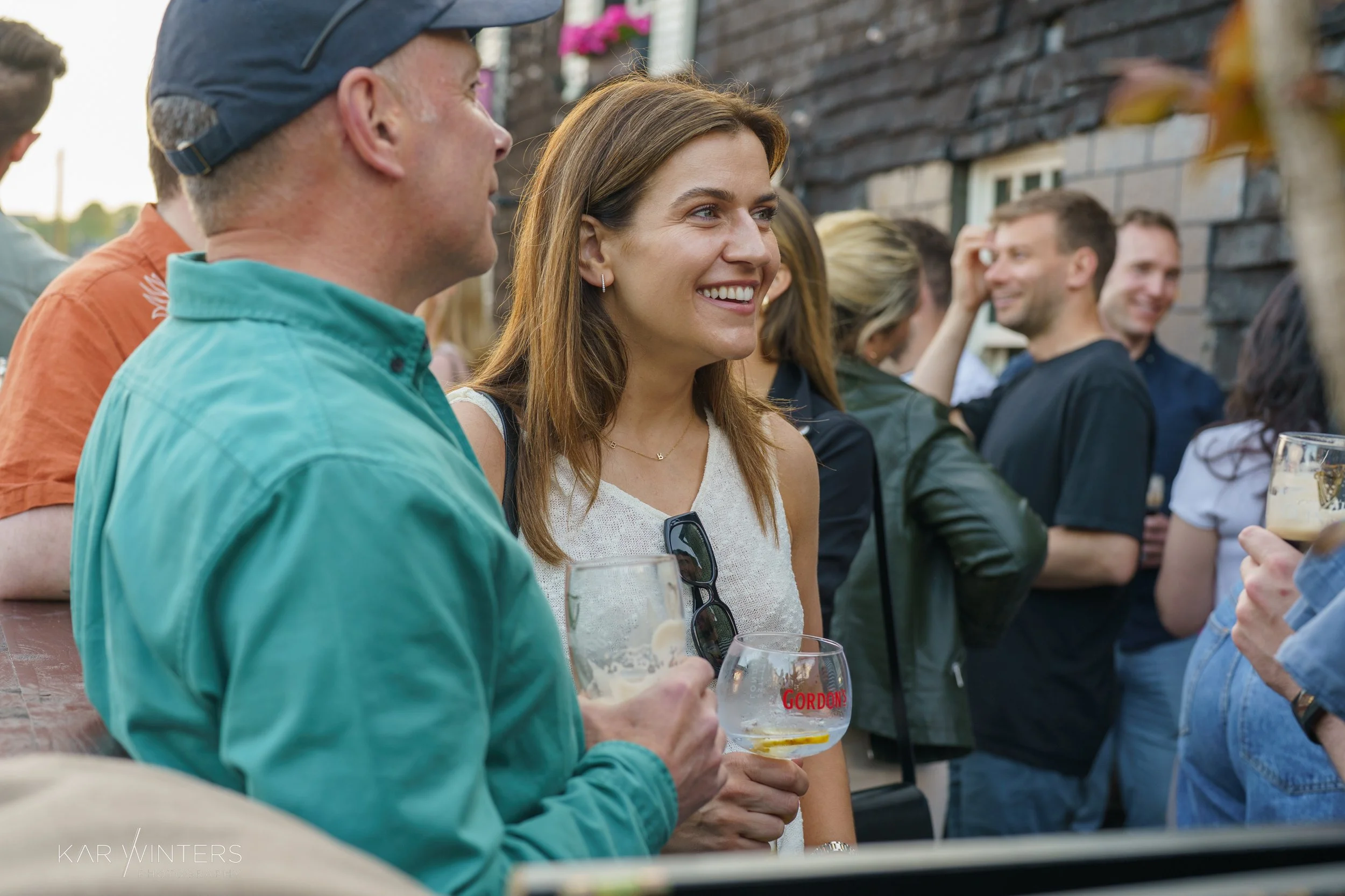 A group of people socializing outdoors, with a woman smiling while holding a glass of beer.