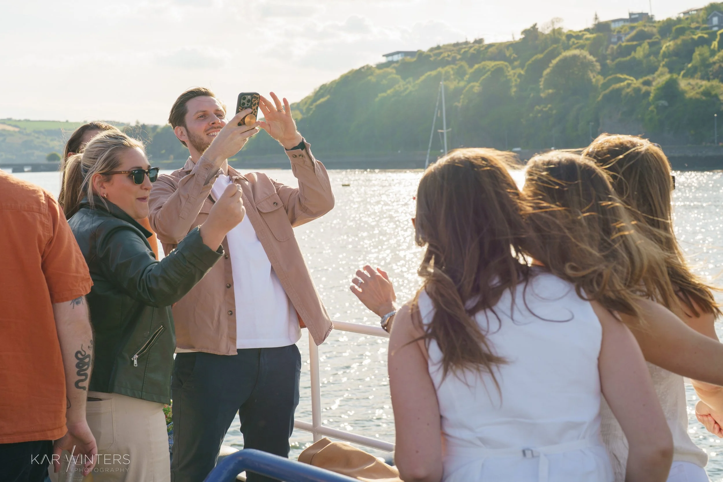 Group of people taking a photo on a boat with water and green hills in the background.
