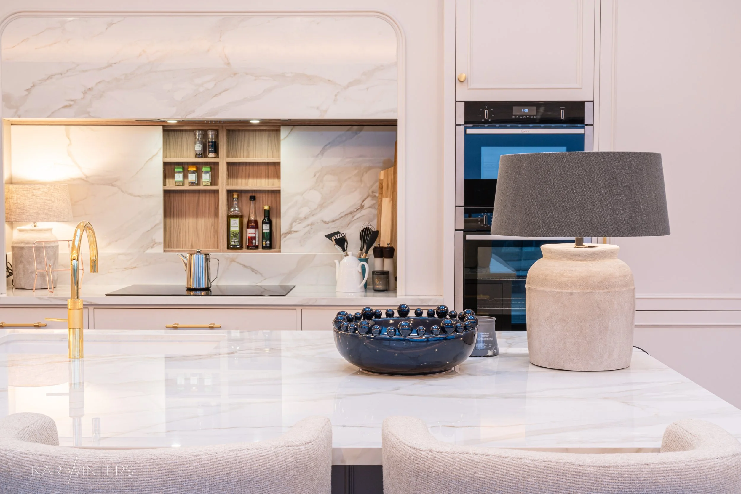 Modern kitchen with marble countertops, a black bowl filled with blueberries on the island, a contemporary table lamp, and kitchen essentials in the background.