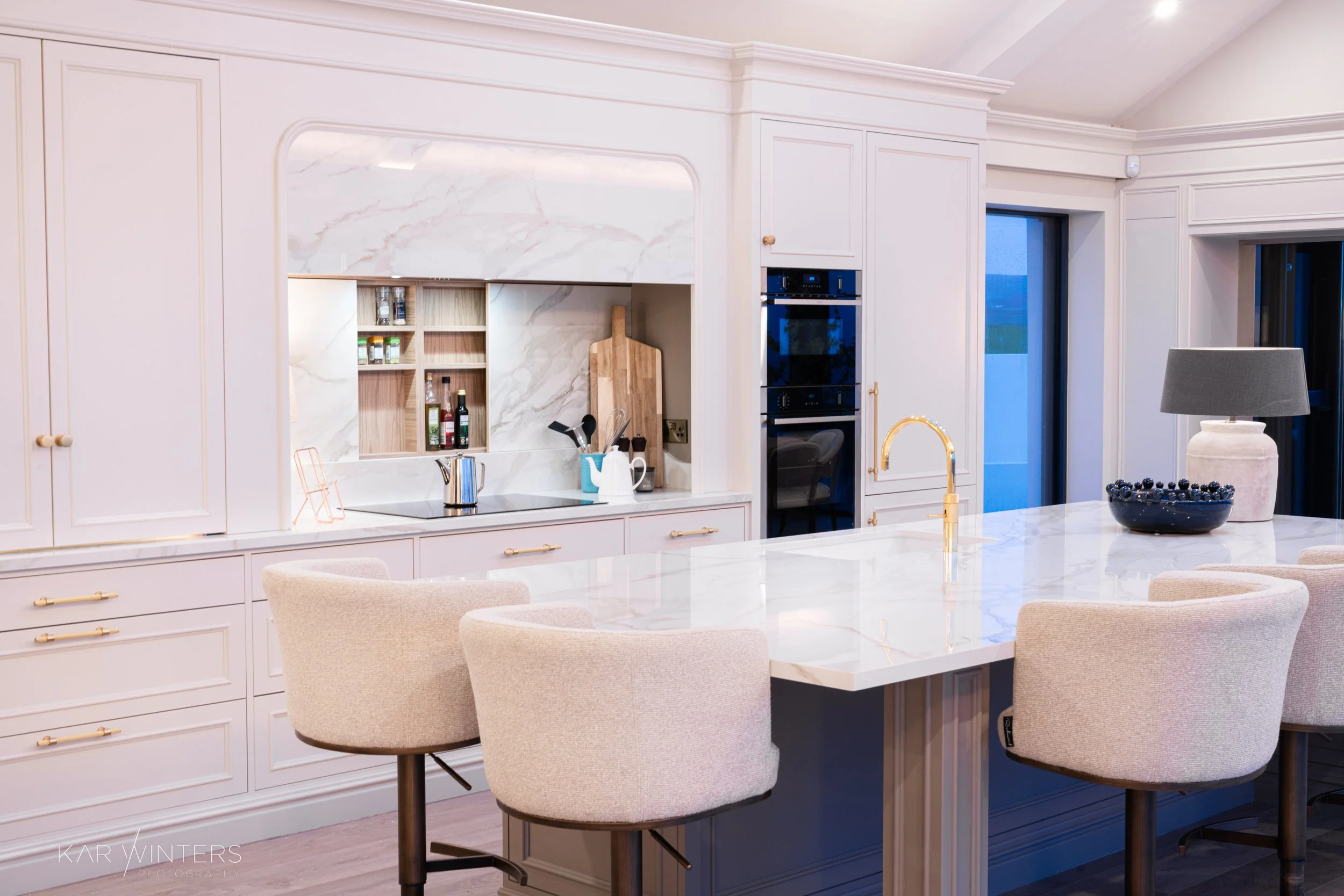 Modern kitchen with white cabinetry, a large marble island, black appliances, and a gray lampshade on a table.