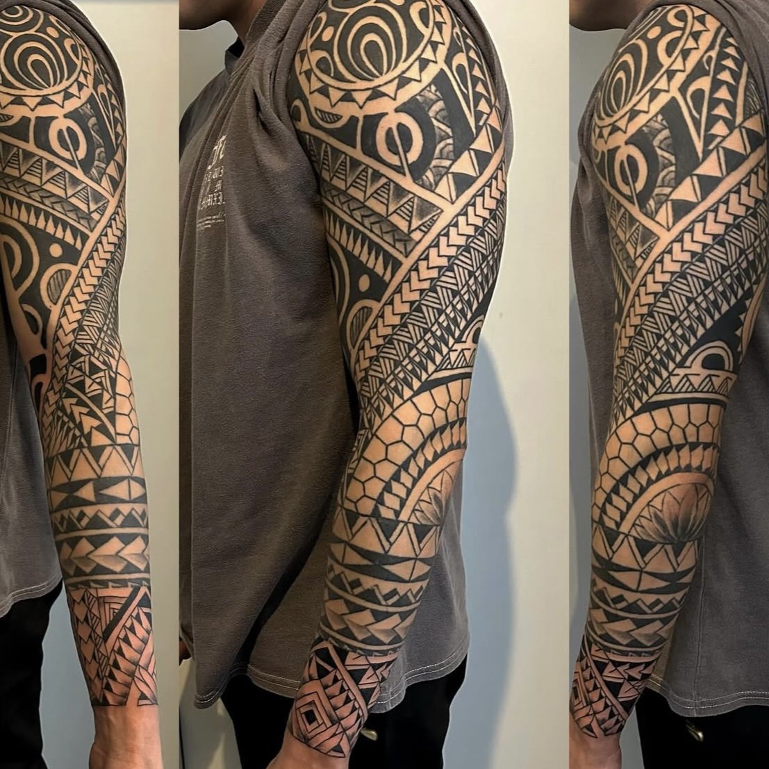 A person with a full sleeve tattoo in traditional Polynesian style, featuring geometric patterns and intricate black ink designs.