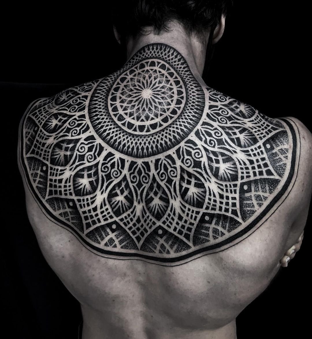 Intricate geometric tattoo on a person's upper back, featuring patterns of circles, curves, and grids, primarily in black ink on a pale skin background.